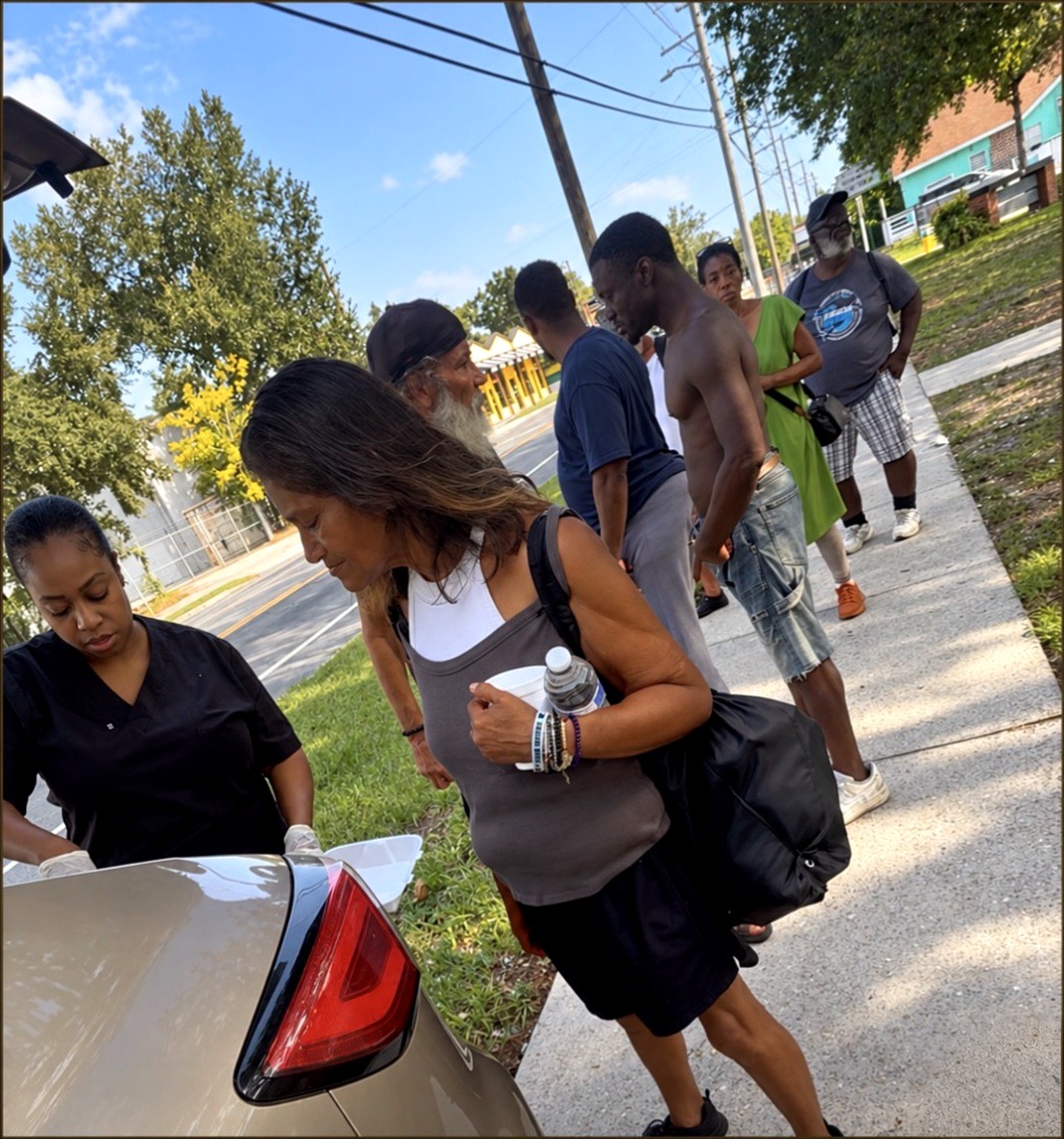 Chef Candy serving hot meals and drinks to neighbors from a car trunk during a Candy Cares outreach