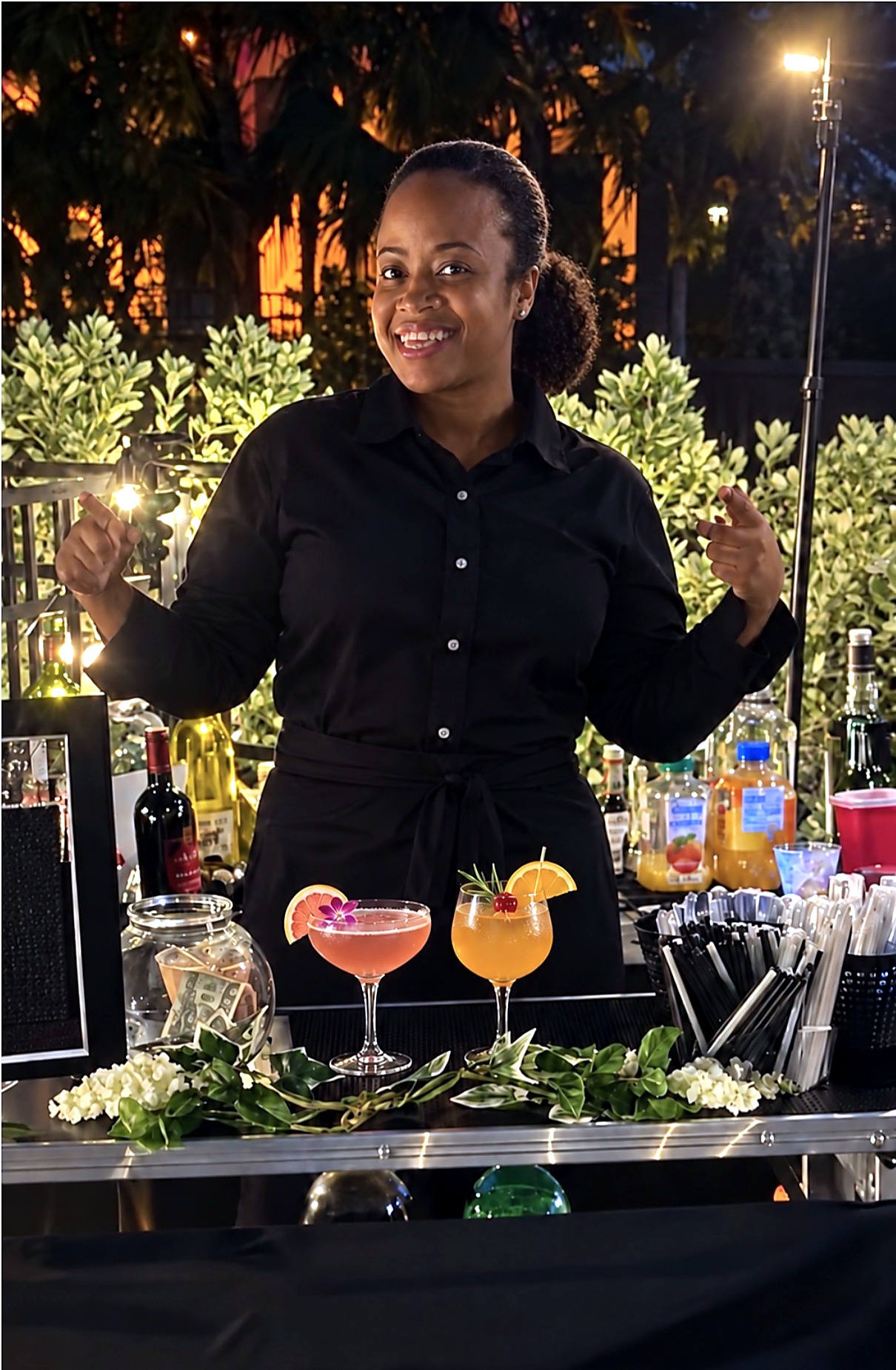 Chef Candy smiling behind her mobile bar at an evening event, two garnished cocktails on the bar mat
