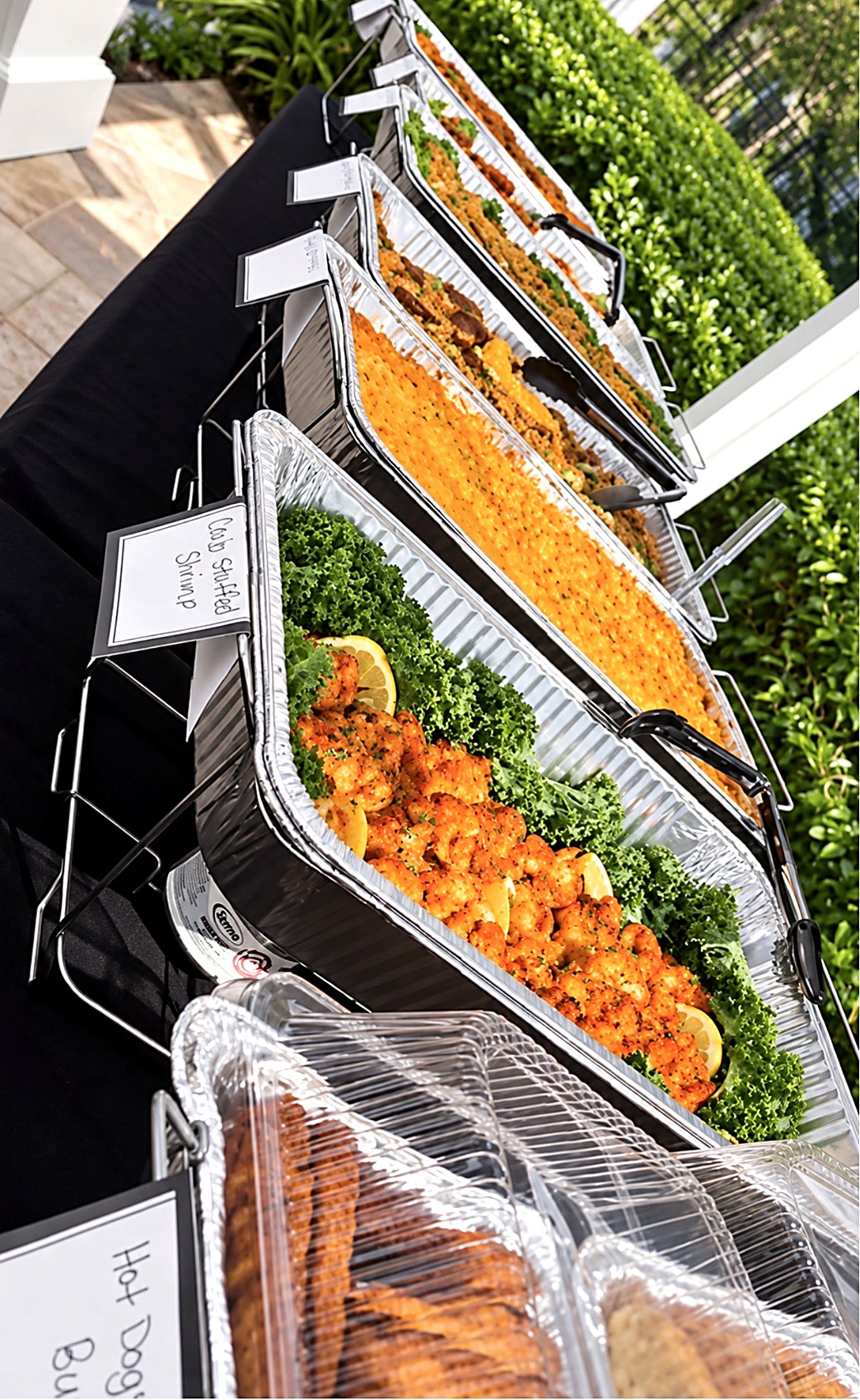 Candy's Southern Flavors catering buffet outdoors: labeled chafing dishes with crab stuffed shrimp and other Southern dishes on a black-draped table.